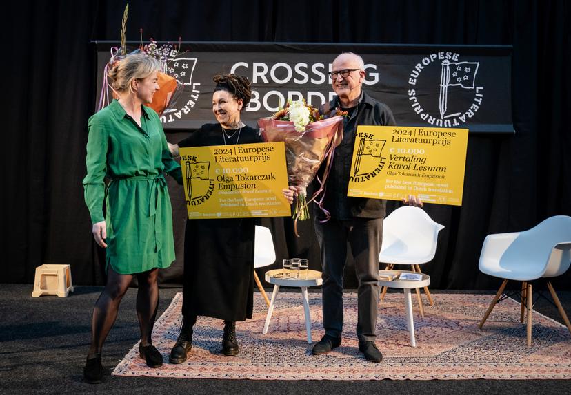 Lachende Romkje met Olga en Karol op een podium, die allebei een cheque vasthouden
